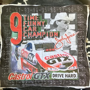 May include: A white cotton bandana with a black border and a colorful design featuring a race car, a driver, and the text "Castrol GTX Drive Hard". The car is a black and red Mustang with the number 9 on the side. The driver is wearing a white hat and sunglasses. The text "Time Funny Car Champion John Force" is also on the bandana.