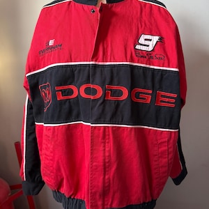 May include: Red and black racing jacket with the word "DODGE" across the chest. The jacket has white accents, a black collar, and the number "9" on the right chest. The Evernham Motorsports logo is on the left chest.