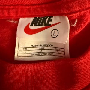 May include: Close-up of a red t-shirt with a Nike label. The label is white with the Nike logo in red and the size is L. The label also includes the text "MADE IN MEXICO" and care instructions.