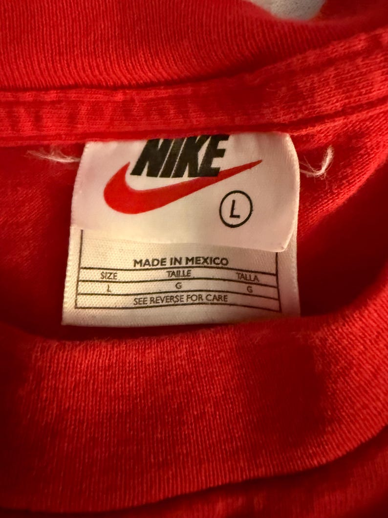 May include: Close-up of a red t-shirt with a Nike label. The label is white with the Nike logo in red and the size is L. The label also includes the text "MADE IN MEXICO" and care instructions.