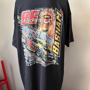 May include: Black t-shirt featuring a colorful graphic of a race car and driver. The design includes the name "Ronnie Basham" and the number "86" in red and yellow. The shirt also has the text "Marksville, Indiana."