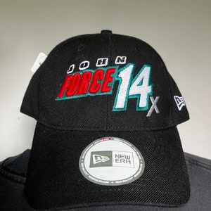 May include: Black baseball cap with a white and green embroidered logo that says "John Force 14x" on the front. The cap has a New Era logo on the side.