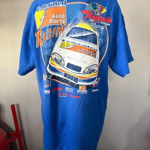 Puede incluir: Camiseta azul con un diseño de coche de carreras y el texto "Federated Auto Parts Racing". El gráfico incluye un coche de carreras, una bandera a cuadros y logotipos de patrocinadores. La camiseta es de cuello redondo y manga corta.