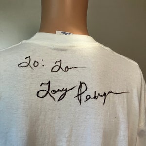 May include: White t-shirt with black writing on the back. The writing says "20:20" and "Tony Parker".
