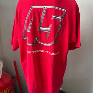 May include: Red t-shirt featuring a large silver and white number 45 on the back. The text "adam petty.com" is printed below the number. The shirt is displayed on a mannequin.