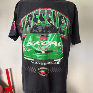 Könnte beinhalten: Schwarzes T-Shirt mit einem grünen Rennwagen-Motiv, dem Text "PRESSLEY" darüber und "SKOAL BANDIT" darunter. Es zeigt auch "MONTE CARLO" und ein Rennlogo. Das T-Shirt wird auf einer Schaufensterpuppe präsentiert.
