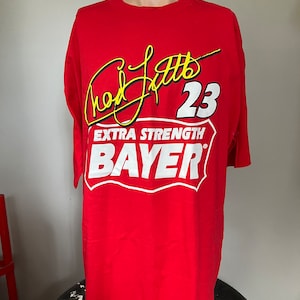 May include: Red t-shirt with a white and yellow graphic of a signature, the number 23, and the text "EXTRA STRENGTH BAYER".