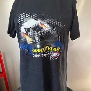 Pode incluir: Camiseta preta com um gr&aacute;fico de um carro de corrida com chamas e o texto "Goodyear Official Tire of NHRA".