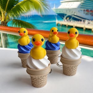 May include: Four keychains shaped like ice cream cones topped with yellow rubber ducks. Two cones feature white soft-serve swirls, while the other two have blue swirls. Each cone has a textured waffle pattern and a small metal ring attached at the base.