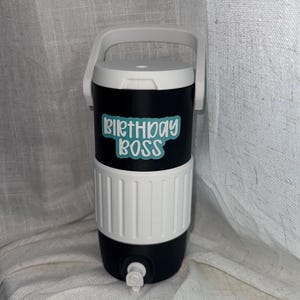 Puede incluir: Enfriador de bebidas aislado en blanco y negro con asa y tapa blancas. El enfriador tiene el texto "BIRTHDAY BOSS" en azul claro. Tiene un grifo para dispensar bebidas.