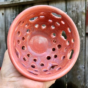 Puede incluir: Un cuenco de cer&aacute;mica de color terracota con un dise&ntilde;o &uacute;nico que presenta un gran agujero central y agujeros m&aacute;s peque&ntilde;os alrededor del borde. El cuenco tiene un esmalte moteado y una superficie ligeramente texturizada.