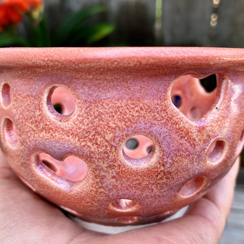 Puede incluir: Un cuenco de cer&aacute;mica rosa con un esmalte moteado y dise&ntilde;os recortados en forma de coraz&oacute;n y c&iacute;rculo. El cuenco tiene una base blanca.