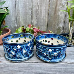 May include: Two round ceramic planters with matching saucers, featuring a deep blue glaze with white highlights. The sides of the planters have a cut-out lattice pattern with circular holes, revealing a smooth, light-colored interior surface.