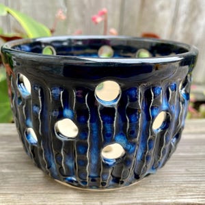 May include: A dark blue ceramic planter with a textured surface and multiple holes. The planter is glazed with a glossy finish.