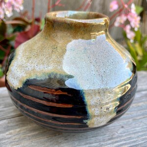May include: A small, round ceramic vase with a narrow opening. The vase has a colour palette of brown, black, and white, with horizontal bands of dark brown and black near the base. The top has a speckled, light brown and white finish.