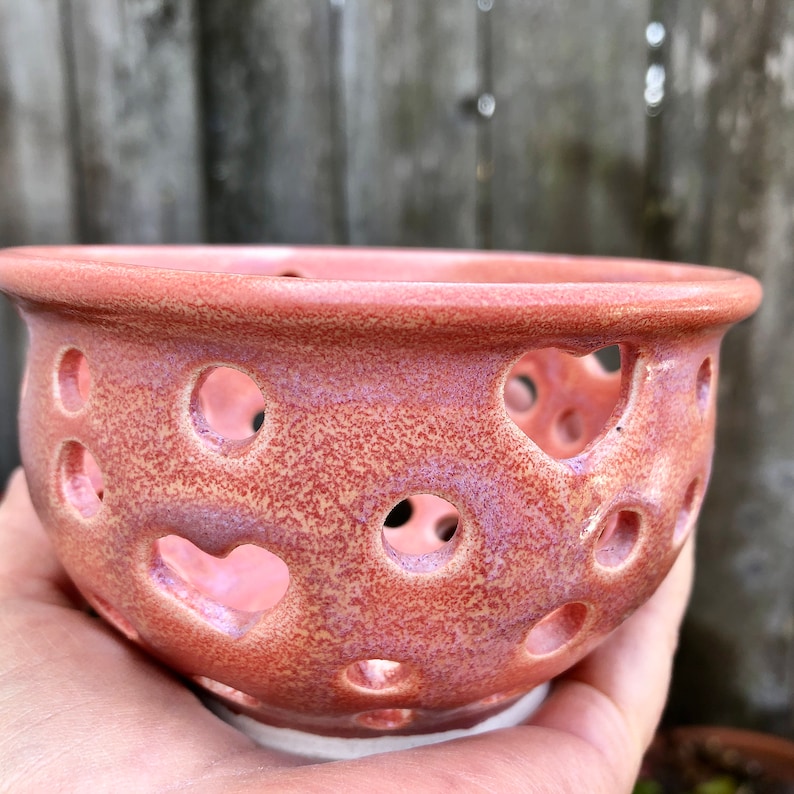Puede incluir: Un cuenco de cer&aacute;mica rosa con un esmalte moteado y recortes en forma de coraz&oacute;n. El cuenco est&aacute; hecho a mano y tiene un aspecto r&uacute;stico y vintage.