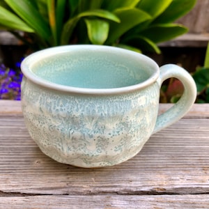 May include: A light blue ceramic mug with a textured, speckled glaze. The mug has a rounded body and a handle.