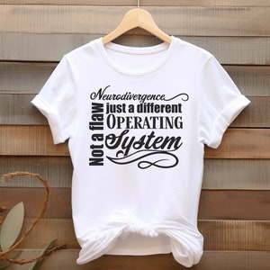 Könnte beinhalten: Weißes T-Shirt mit dem Text "Neurodivergence just a different OPERATING System" in Schwarz. Der Satz "Not a flaw" ist vertikal auf der linken Seite aufgedruckt. Das T-Shirt hängt an einem Holzbügel.