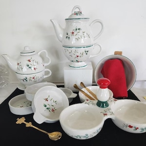May include: A white tea set with a holly and berry pattern. The set includes a teapot, two cups, a creamer, a sugar bowl, and a set of two small bowls with a spoon.