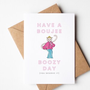 May include: A greeting card with a cartoon cat wearing a pink jacket and blue and white striped pants. The text on the card reads "Have a Boujee Boozy Day [You Deserve It]"