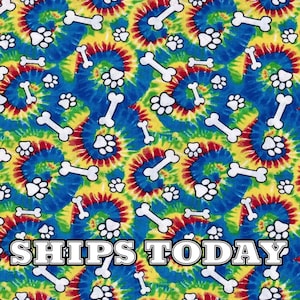 May include: A colorful tie-dye fabric with a repeating pattern of white paw prints and bone shapes. The fabric has a blue, yellow, red, and green color scheme. The text "SHIPS TODAY" is printed in white letters on the bottom of the fabric.