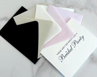 Pode incluir: Uma pilha de envelopes quadrados nas cores preto, creme e rosa pálido. O envelope branco superior apresenta o texto impresso em preto, "THERE AIN'T NO PARTY LIKE A Bridal Party," escrito em uma combinação de fontes sem serifa e manuscrita elegante.