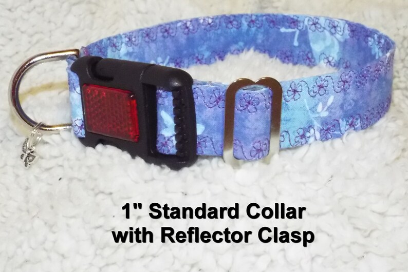 May include: A 1 inch wide blue and purple floral dog collar with a silver D-ring and a black buckle with a red reflector. The text "1" Standard Collar with Reflector Clasp" is printed below the collar.