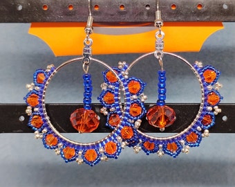 Könnte beinhalten: Ein Paar Creolen mit blauen und orangefarbenen Perlen. Die Ohrringe sind aus Silberdraht gefertigt und haben eine baumelnde Kristallperle am unteren Ende.