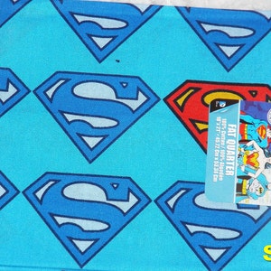 May include: A blue fabric with a repeating pattern of Superman logos. The fabric is labeled as a "Fat Quarter" and measures 18 inches by 21 inches (45.72 cm x 53.34 cm).