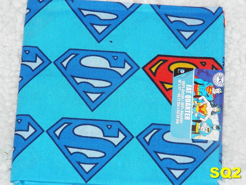 May include: A blue fabric with a repeating pattern of Superman logos. The fabric is labeled as a "Fat Quarter" and measures 18 inches by 21 inches (45.72 cm x 53.34 cm).