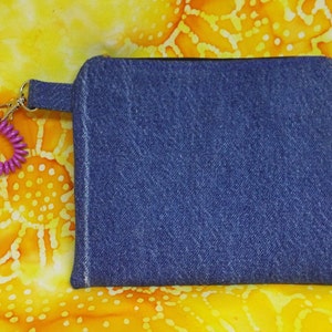 May include: A small blue denim pouch with a zipper closure and a pink hair tie attached to a silver key ring.