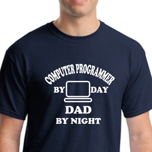 Puede incluir: Una camiseta azul marino con texto blanco que dice "Computer Programmer by Day Dad by Night". La camiseta presenta un contorno blanco de un ordenador portátil.