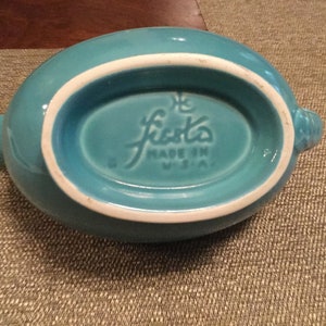 May include: Turquoise blue Fiestaware gravy boat with a white rim and the words "Fiesta Made in U.S.A." on the bottom.