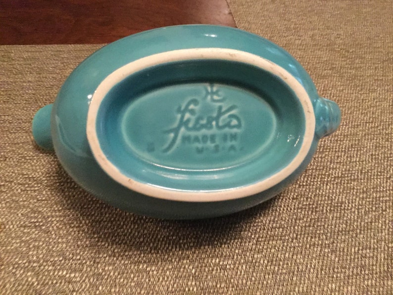 May include: Turquoise blue Fiestaware gravy boat with a white rim and the words "Fiesta Made in U.S.A." on the bottom.
