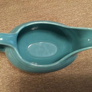 May include: A turquoise blue ceramic gravy boat with a smooth, rounded interior and a slightly flared lip. The boat has a single handle on the left side.
