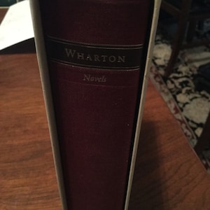 May include: A burgundy book with a white spine and the title "WHARTON Novels" on the front cover.