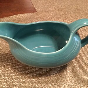 May include: A teal blue ceramic gravy boat with a wide, rounded base and a single handle.