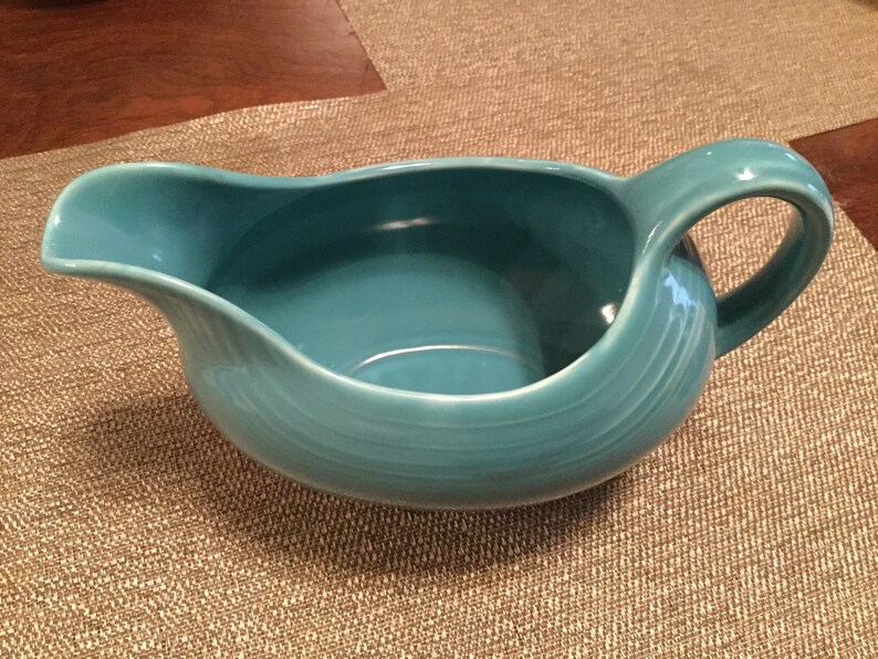 May include: A teal blue ceramic gravy boat with a wide, rounded base and a single handle.