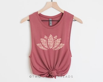 May include: A dusty rose sleeveless tank top with a white lotus flower graphic. The graphic is made up of smaller white flowers. The tank top is knotted at the bottom and has the text "TWO JADE THREADS" at the bottom.