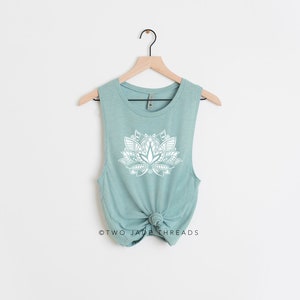 Puede incluir: Una camiseta sin mangas de color azul claro con un dise&ntilde;o de flor de loto blanca. La camiseta est&aacute; anudada en la parte inferior y tiene el texto "TWO JADE THREADS" en la parte inferior.