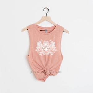 Puede incluir: Un top sin mangas de color melocot&oacute;n con un dise&ntilde;o de flor de loto blanca. El top est&aacute; en una percha y tiene el texto "TWO JACK THREADS" en la parte inferior.