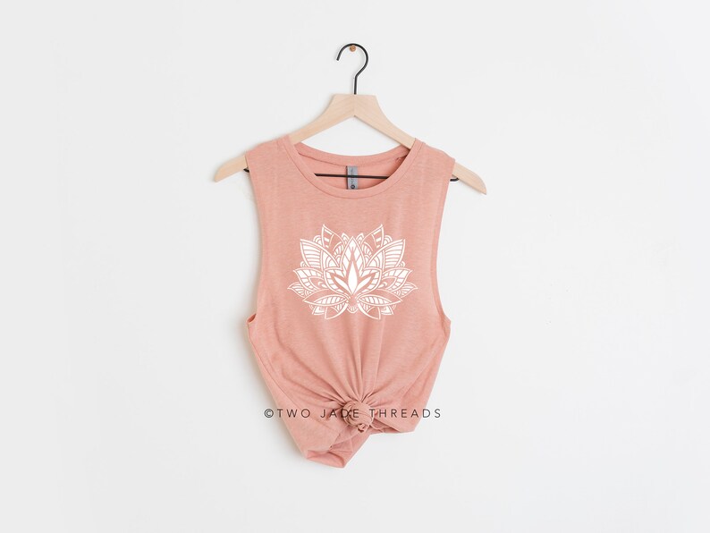 Puede incluir: Un top sin mangas de color melocot&oacute;n con un dise&ntilde;o de flor de loto blanca. El top est&aacute; en una percha y tiene el texto "TWO JACK THREADS" en la parte inferior.