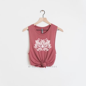 Puede incluir: Un top sin mangas de color rosa polvoriento con un gr&aacute;fico de flor de loto blanca. El top est&aacute; atado en la parte inferior y tiene el texto "TWO JADE THREADS" en la parte inferior.
