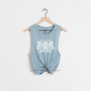 Puede incluir: Un top sin mangas de color azul claro con un dise&ntilde;o de mandala blanco en forma de flor de loto. El texto "TWO JADA THREADS" est&aacute; impreso en la parte inferior de la camiseta.
