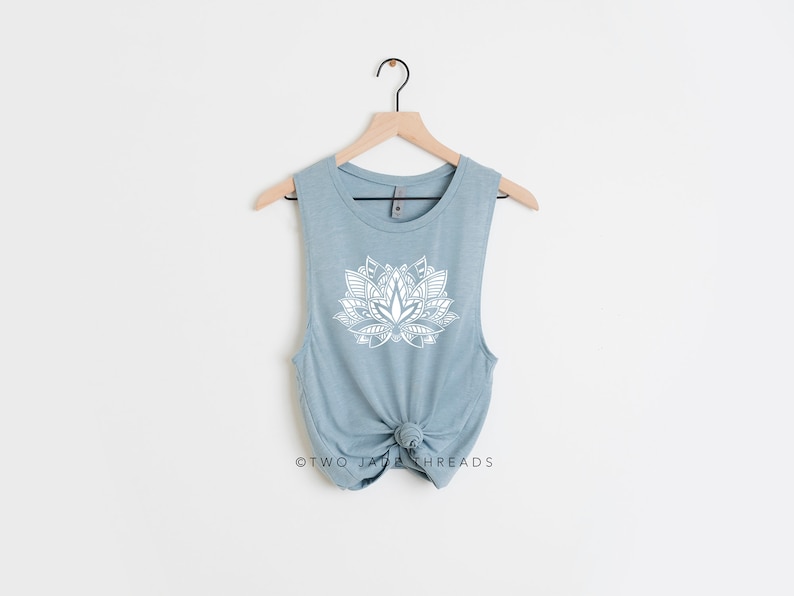 Puede incluir: Un top sin mangas de color azul claro con un dise&ntilde;o de mandala blanco en forma de flor de loto. El texto "TWO JADA THREADS" est&aacute; impreso en la parte inferior de la camiseta.