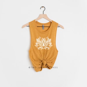 Puede incluir: Un top sin mangas de color amarillo mostaza con un dise&ntilde;o de mandala de flor de loto blanco. El top est&aacute; anudado en la parte inferior y tiene un ajuste holgado.
