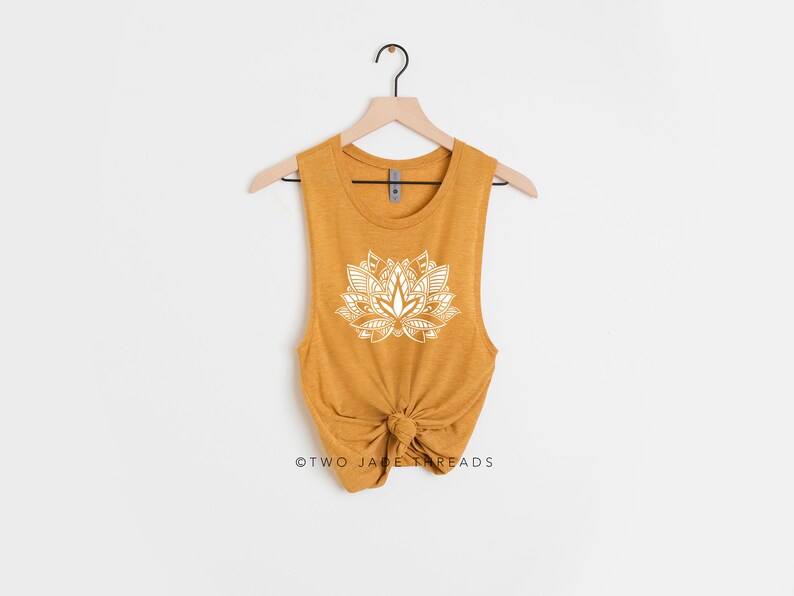 Puede incluir: Un top sin mangas de color amarillo mostaza con un dise&ntilde;o de mandala de flor de loto blanco. El top est&aacute; anudado en la parte inferior y tiene un ajuste holgado.