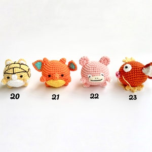 May include: Four crocheted figures in a row. The first is yellow and white, the second is orange with blue accents, the third is pink, and the fourth is orange with a white fin. Each has a number below it.