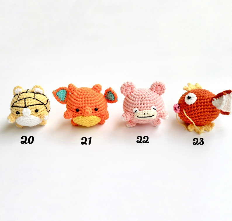 May include: Four crocheted figures in a row. The first is yellow and white, the second is orange with blue accents, the third is pink, and the fourth is orange with a white fin. Each has a number below it.