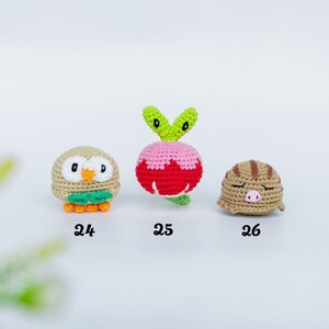 May include: Three crocheted amigurumi figures: an owl, a radish, and a sleeping pig. The owl is tan with orange feet and green accents. The radish is pink and red with green leaves. The pig is tan with brown stripes.